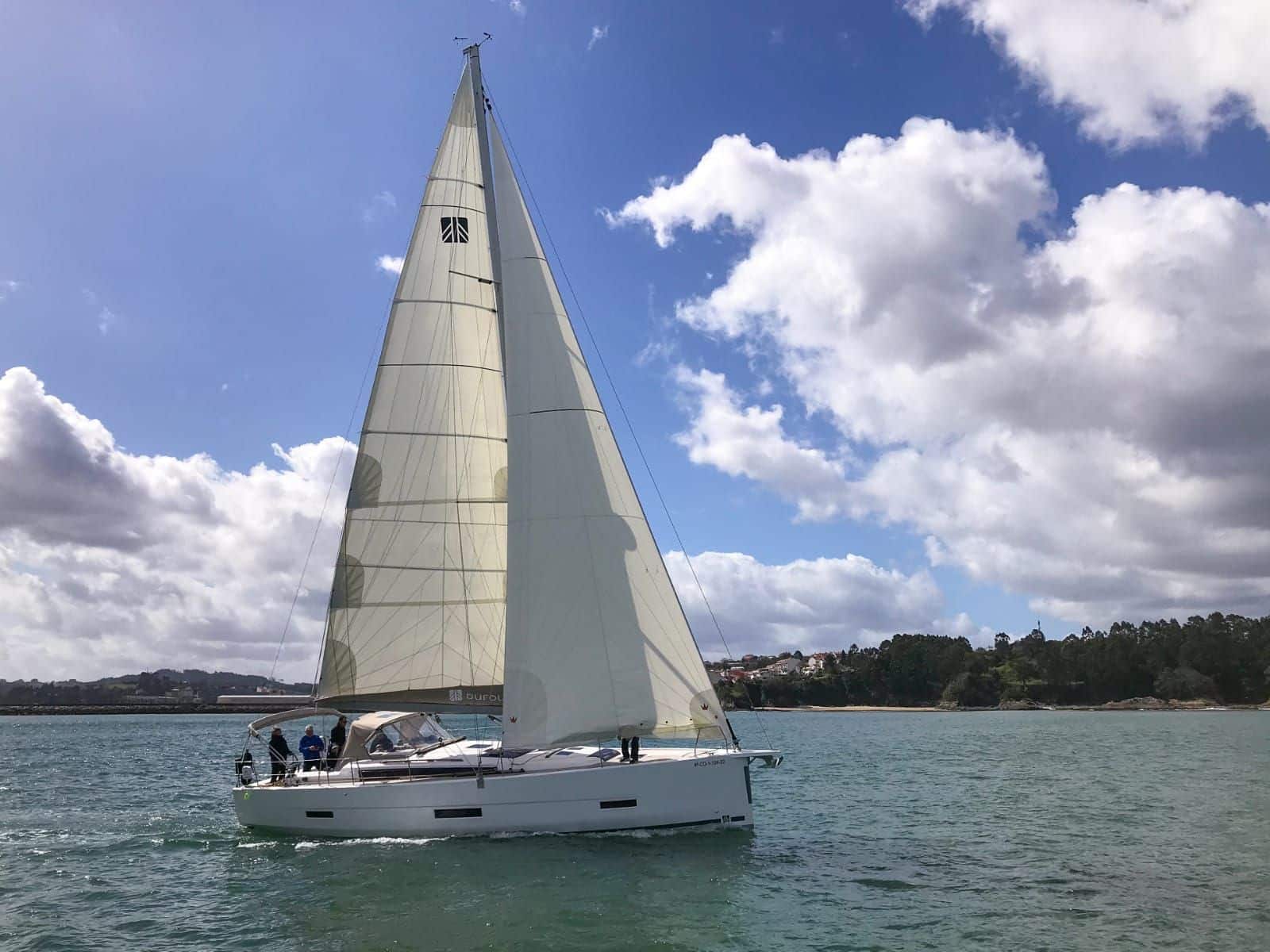 Cuatro personas navegando por las Rías Baíxas en el velero Amodiño un día soleado con nubes