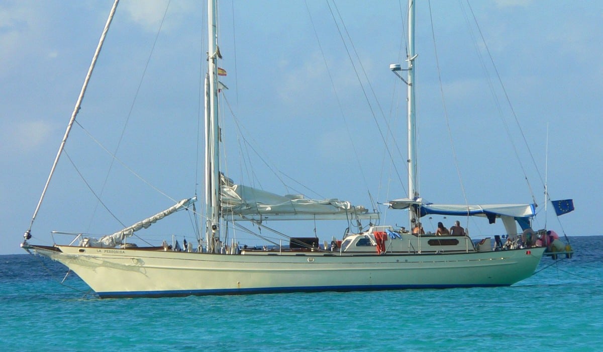 Velero La Peregrina fondeado en el mar con tres personas en él disfrutando de un día soleado